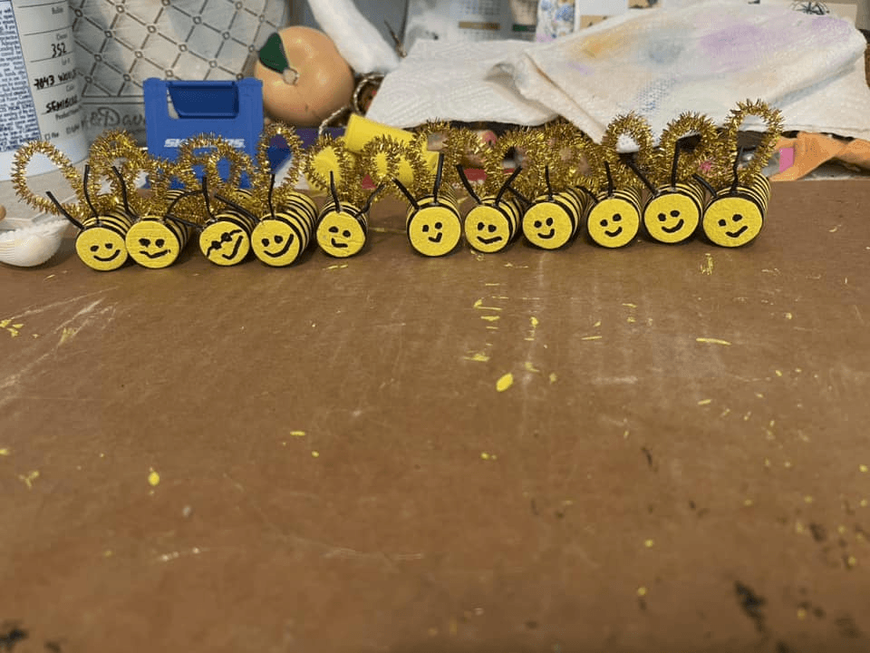 DIY bee decorations made from pipe cleaners and foam circles on a crafting table.