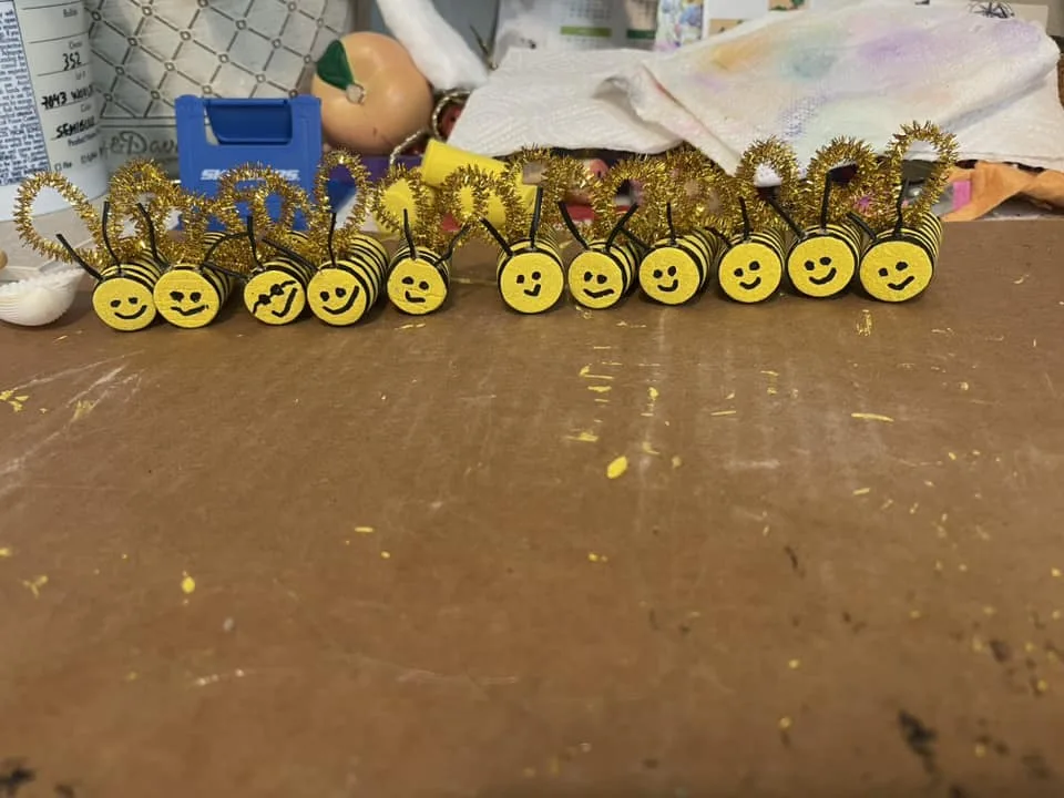 DIY bee decorations made from pipe cleaners and foam circles on a crafting table.