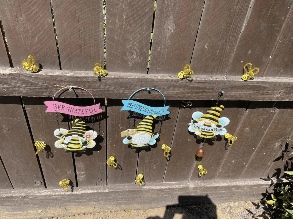 Cute bee decorations hanging on a garden fence.