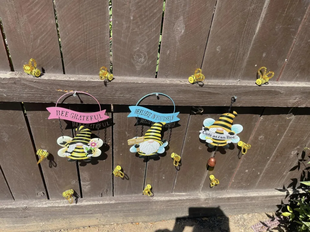 Cute bee decorations hanging on a garden fence.