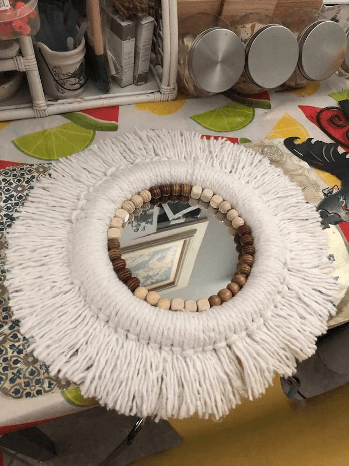 A DIY boho-style mirror made with a Dollar Tree mirror, string mop fringe, and wooden beads, creating a stylish and earthy home decor piece.