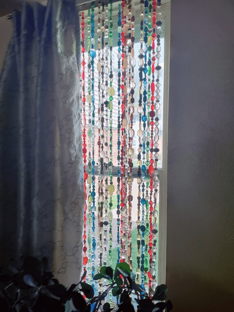 A colorful DIY beaded curtain hanging in a window, made with an assortment of vibrant beads strung on fishing line.