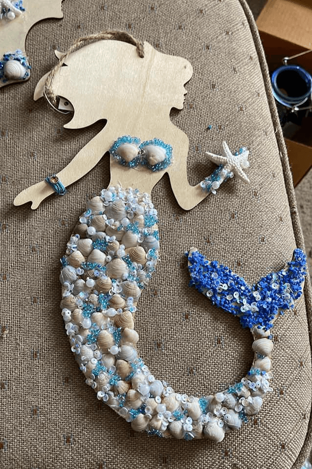 A DIY mermaid wall decor piece made with a wooden cutout, seashells, and beads, creating a beautiful and beachy decorative item.