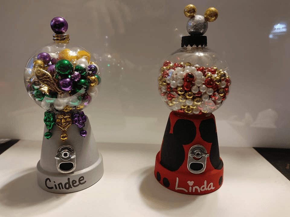 DIY gift jars made with clay pots, clear Christmas bulbs, and colorful beads, personalized with names on the base and decorated in festive colors.