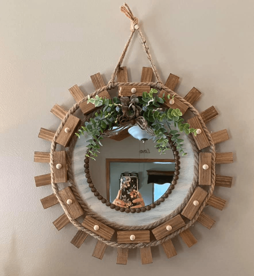 sunburst mirror featuring wooden accents, jute rope, and decorative beads, adorned with faux greenery for a cozy, rustic look.