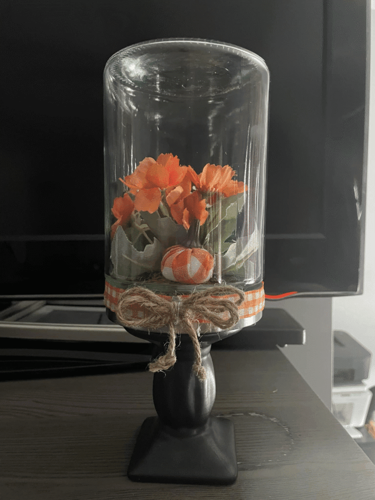 DIY fall cloche display made from an upside-down glass vase with faux flowers, pumpkin, ribbon, and twine bow