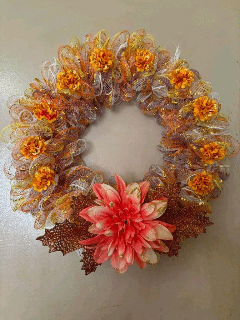DIY fall wreath made with mesh ribbon, orange and pink faux flowers, and glittered leaves