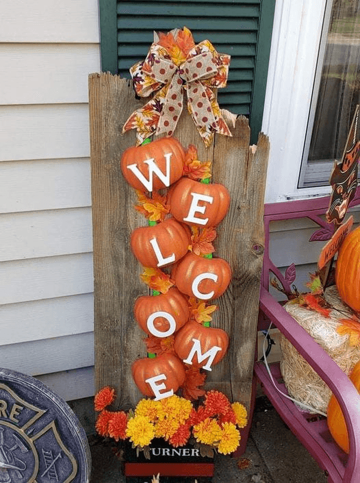 DIY fall porch sign made with pumpkins, WELCOME letters, and autumn leaves on a wooden board